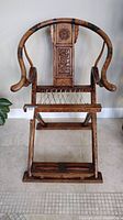 Full front view of wooden folding chair showing horseshoe back, carved back panel, cord seat and foot roller base