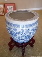 Front close-up of the Asian ceramic planter showing blue floral and leaf design with decorative rim and wooden stand.