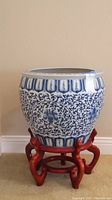 Front view of blue and white Asian ceramic planter on red carved wooden stand showing patterns and shape.