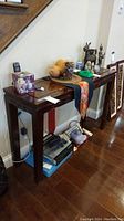 Full view of the wood console table showing the top, apron with carved design, and tapered legs. Various items on top and underneath the table are not included.