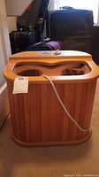 Wooden foot sauna unit with dual foot openings and a cloth lining for feet. Power cord visible.