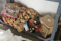 Shelf view showing large ornate gold-toned carved wood decorative pieces, ceramic creamer and sugar bowl on a wooden stand, a cardboard box, and a framed heart-shaped textile decoration with dried flowers.