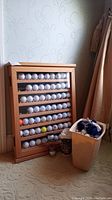 Wide view of the wooden display rack with multiple rows of golf balls arranged inside on shelves, located near a curtain.