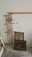 Full view of the macrame wall hanging alongside the two Asian decorative carved panels on the floor against a wall.