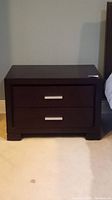 Front view of dark brown MDF nightstand with two closed drawers and silver handles.