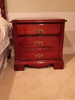 Front view of the nightstand showing three drawers with decorative brass handles and scalloped base.