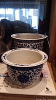 Two blue and white ceramic plant pots with floral Asian style pattern shown from side. Both placed on calendar with one slightly inside the other.