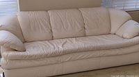 Front view of white leather-like sofa showing three seat cushions and padded arms