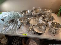 Overview of stainless steel pots and pans with handles, wrapped in plastic.