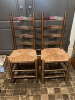 Front view of two wooden ladder back chairs with woven rattan seats placed side by side on tiled floor.