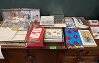 Wide view of assorted Christmas cards and packs spread on a wooden dresser.