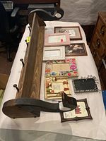 Photo of wooden shelf with Canadian geese shaped end caps and several hooks beneath, displayed alongside various picture frames of different styles and sizes on a bed.
