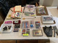 Overview of all lot items laid out on a table including gel pens, cards, notebooks, calculator, and clips.