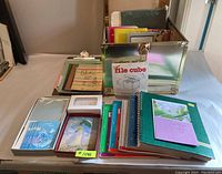 Photo showing gold metal file box filled with various notebooks and folders on a table with sets of cards and stationery laid out in front.