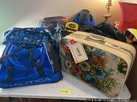 Photo showing a table with multiple bags including a blue Nautica duffel bag, MEC orange and gray bag, and bags possibly containing snorkel gear.