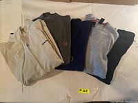 Five Tommy Hilfiger sweaters and jackets laid flat, showing color and general style of each item.