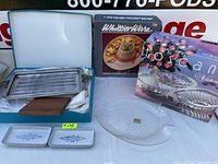 View of the metal serving tray in blue box, WhittierWare boxed nacho hat platter, and clear glass serving bowl in original boxes with two rectangular blue floral ceramic dishes.
