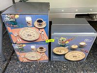 Four boxes of stoneware sets by Jinter National with colorful village pattern on beige background.
