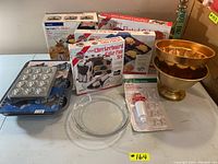 Full view of the lot showing boxed and loose bakeware items including pie maker, mixing bowls, cake pans and measuring accessories.