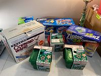 Multiple unopened Ziploc brand food storage container packs and bags in original packaging alongside boxed Corning Ware saucepot.