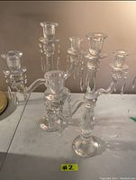 Pair of clear crystal candle holders with three arms each and hanging crystal prisms, shown on a table with neutral background.