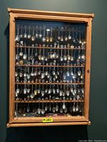 Front view of the wooden display case filled with decorative spoons hung on wooden rods across multiple shelves.