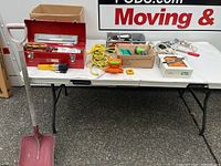 Overview of tools and items displayed on a table, including a red metal toolbox filled with hand tools and various loose hardware items and cords.