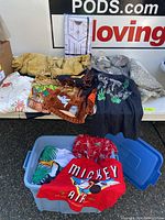 Blue bin containing various vintage clothes and costumes including the Mickey Air top and the toucan print shirt