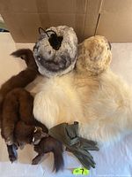 Top view of multiple vintage fur accessories including fur hats, muffs, a brown fur stole with tail, a white fur wrap, and olive green gloves laid out on a surface.