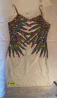 Photo of vintage sequin dress laid flat showing full front with colorful sequin design on top and white textured bottom.