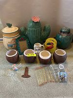 Photo of vintage tropical-themed ceramic items including cactus planter, flamingo figure, cookie jar, lidded jar, pitcher, photo frame and ceramic cup holders.
