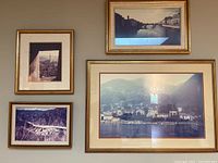Four gold-toned frames arranged on a wall displaying vintage travel-themed photos showing cityscapes and bridges.