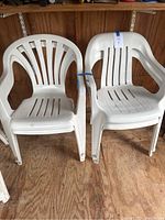 Two different styles of white plastic outdoor chairs side by side stacked in a wooden shed