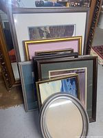 Several framed artworks and mirrors stacked upright showing various sized frames and decorative border styles
