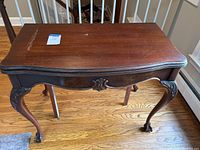 Front view of wooden accent table showing rectangular top with wear and scratch, curved ornate legs and claw feet.