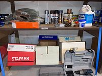 Shelf with cans of spray enamel, wood stains, paint thinner, citronella candles, boxes with miscellaneous items