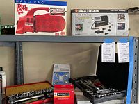 Black & Decker Air Station inflator compressor box, Dirt Devil Hand Vac box, two tool sets, Schwinn tube, Honda wheel locks on metal shelving