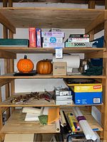 Wooden shelving unit holding board games including Checkers, Sorry, All of Us, America, pumpkin decorations, golf ball box, laundry box, paper rolls, and miscellaneous items.