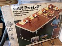 Box for folding table with product image showing the table seats 8, size 24x60 inches, easy to clean oak vinyl on fiberwood, aluminum edged