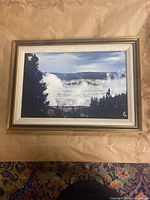 Photo of a framed landscape artwork depicting misty forest and hills in a gold-tone frame with inner white mat