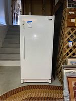 Front angle view of white Frigidaire upright freezer showing door, handle, and control panel.