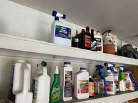 Two shelves with various plastic bottles and containers of gardening chemicals, fertilizers, and multiple types of engine oils and fuel additives.