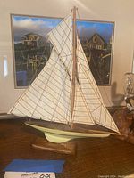 Sailboat model with white sails and cream hull on wooden stand before nautical scene photo.
