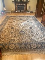 Full view of large rectangular area rug with beige, brown, and blue floral medallion pattern on light background with fringe edges on short ends.