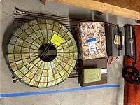 Top-down view showing large stained glass light fixture with metal hanging hooks, floral keepsake box, scale, and projector cases placed on a rug