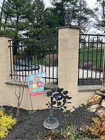 Birdbath and garden flag in backyard garden bed near stone wall and black metal fence