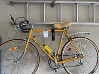 Side view of yellow Panasonic Sport Deluxe road bicycle hanging in garage with aluminum ladder above it