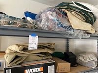Shelf with beige tarps, plastic bags of cups, life preserver, blue tarp, and folded green tarps.