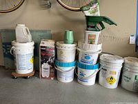 Overview of all buckets of pool care chemicals, boxes, grass seed spreader, and assorted supplies.