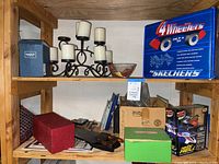 Shelf with Skechers 4 Wheelers roller skates box, candle holder with candles, glass bowl, model car boxes, and other miscellaneous boxed items.